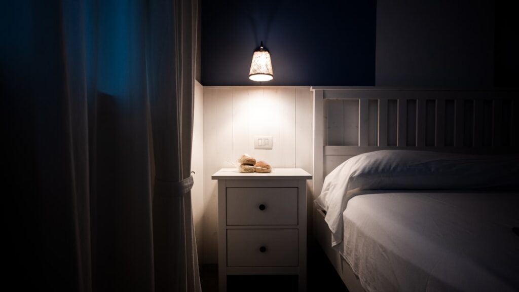 A bedside lamp illuminates a nightstand next to a bed